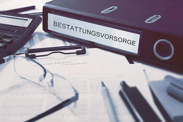 Auf einem Schreibtisch liegt eine Mappe mit der Aufschrift BESTATTUNGSVORSORGE, daneben liegen Dokumente, ein Stift, eine Brille und ein Taschenrechner - ein Zeichen dafür, wie wichtig es ist, mit der Bestattungsvorsorge vorauszuplanen. - Bestattungsunternehmen in Winsen, Harburg und in der Elbmarsch.