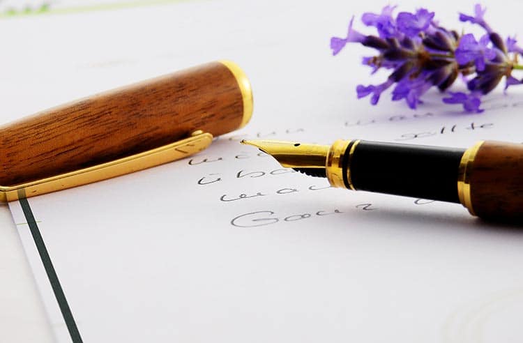 Eine Nahaufnahme eines Füllfederhalters mit Holzkappe, der auf handgeschriebenem Papier liegt, begleitet von einem Zweig violetter Blumen - eine stimmungsvolle Szene, die man oft in Allgemeinen Trauertexten findet. - Bestattungsunternehmen in Winsen, Harburg und in der Elbmarsch.